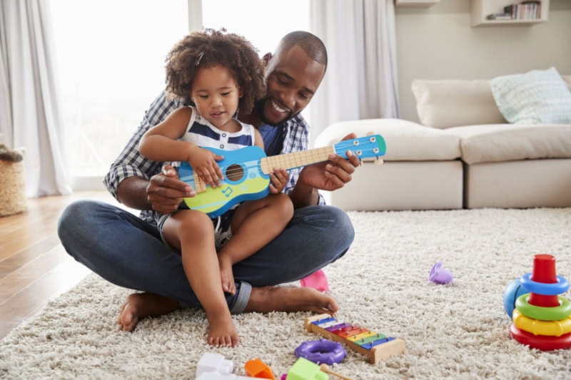 Dad and toddler playing a toy guitar.