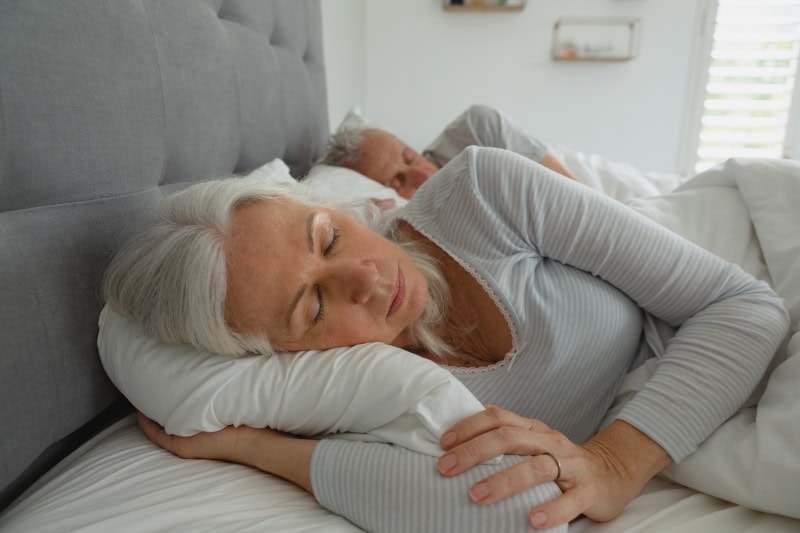 Active senior couple sleeping together in bed in bedroom Front view of active senior Caucasian couple sleeping together in bed in bedroom at home
