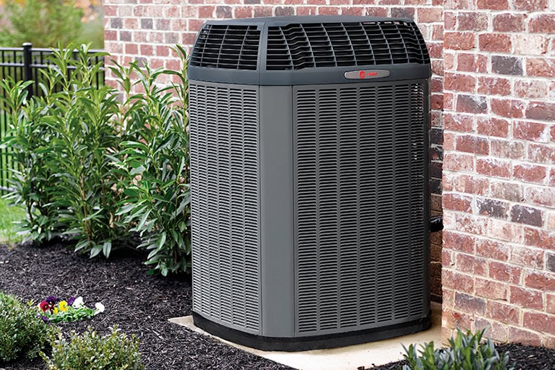3 Tips to Prevent AC Breakdown During a Heat Wave. Photo of a black air conditioning unit installed outside of a brick home.
